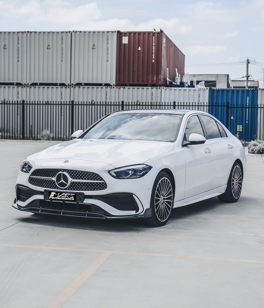 White Mercedes sedan with custom Mars Performance front lip parked in front of shipping containers on a concrete lot.